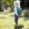 Ein Kind steht mit dem Rücken zur Kamera und trägt einen grünen deuter Pico Kinderrucksack in der Farbe Glacier-dustblue, umgeben von einer sonnigen Wiese.