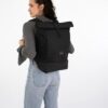 Johnny Urban Rolltop Rucksack in Schwarz, getragen von einer jungen Frau mit braunen Haaren, ideal für Uni, Arbeit und Reisen, mit Laptopfach und Schuhfach, wasserabweisend
