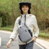 Junge Frau mit grauer Sling Bag unterwegs auf einem Waldweg in sportlicher Kleidung. Die Tasche bietet viel Platz und Funktionalität für Outdoor-Aktivitäten und Reisen.