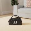 Schwarze Under Armour UA Undeniable 5.0 Duffle SM Backpack Sporttasche auf hellem Teppichboden, ideal für Sport und Reisen.