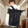 Yooler Rolltop Rucksack in Schwarz, wasserdicht und modern, von hinten getragen in einem urbanen Umfeld, ideal für Schule, Reisen und Freizeit.