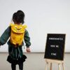 Ein fröhliches Kind mit einem ergonomischen Kindergarten-Rucksack in Tiger-Design, der für 1-3-Jährige geeignet ist. Der Rucksack ist gelb, reflektierend und hat eine praktische Ziehzunge mit Namensschild.