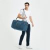 Mann mit dunkelblauer Reisetasche von WANDF, 85L, mit Schuhfach, ideal für sportliche Aktivitäten und Reisen, in hellem Raum stehend.